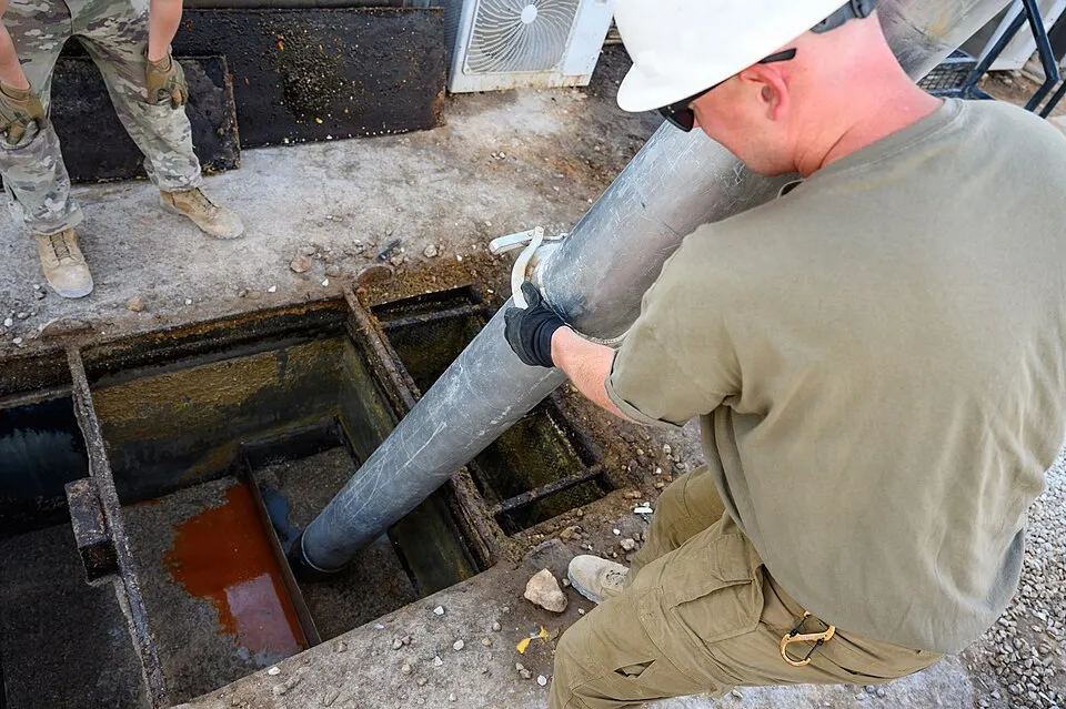 Technician guiding a vacuum hose into an open grease trap